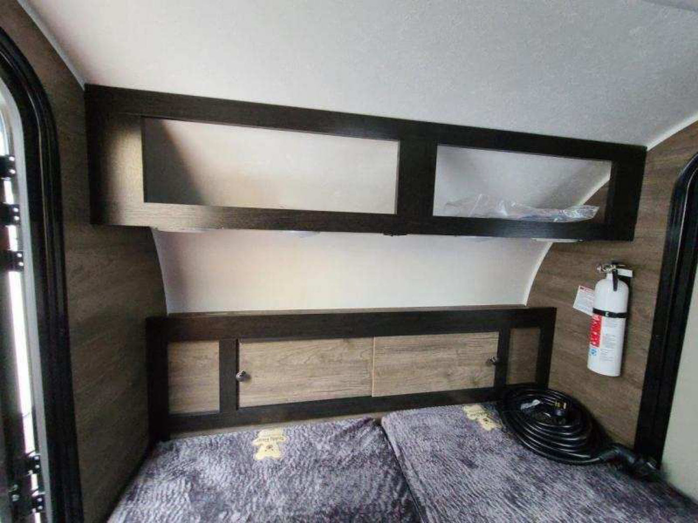 and two mattresses for sleeping.|Spacious RV rental interior featuring a large bed with overhead storage and main entry door.|RV rental interior featuring a compact sleeping area with a textured bed — photo 6
