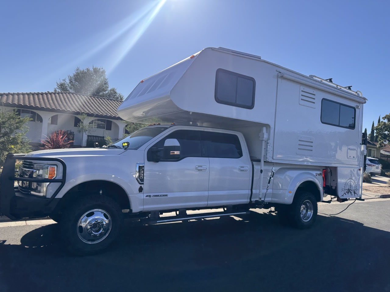 parked on a sunny suburban street.|This large white pickup truck with a spacious truck camper makes an ideal RV rental for any adventure on a sunny day.|Large white truck camper on a Ford dually with off-road gear — photo 3
