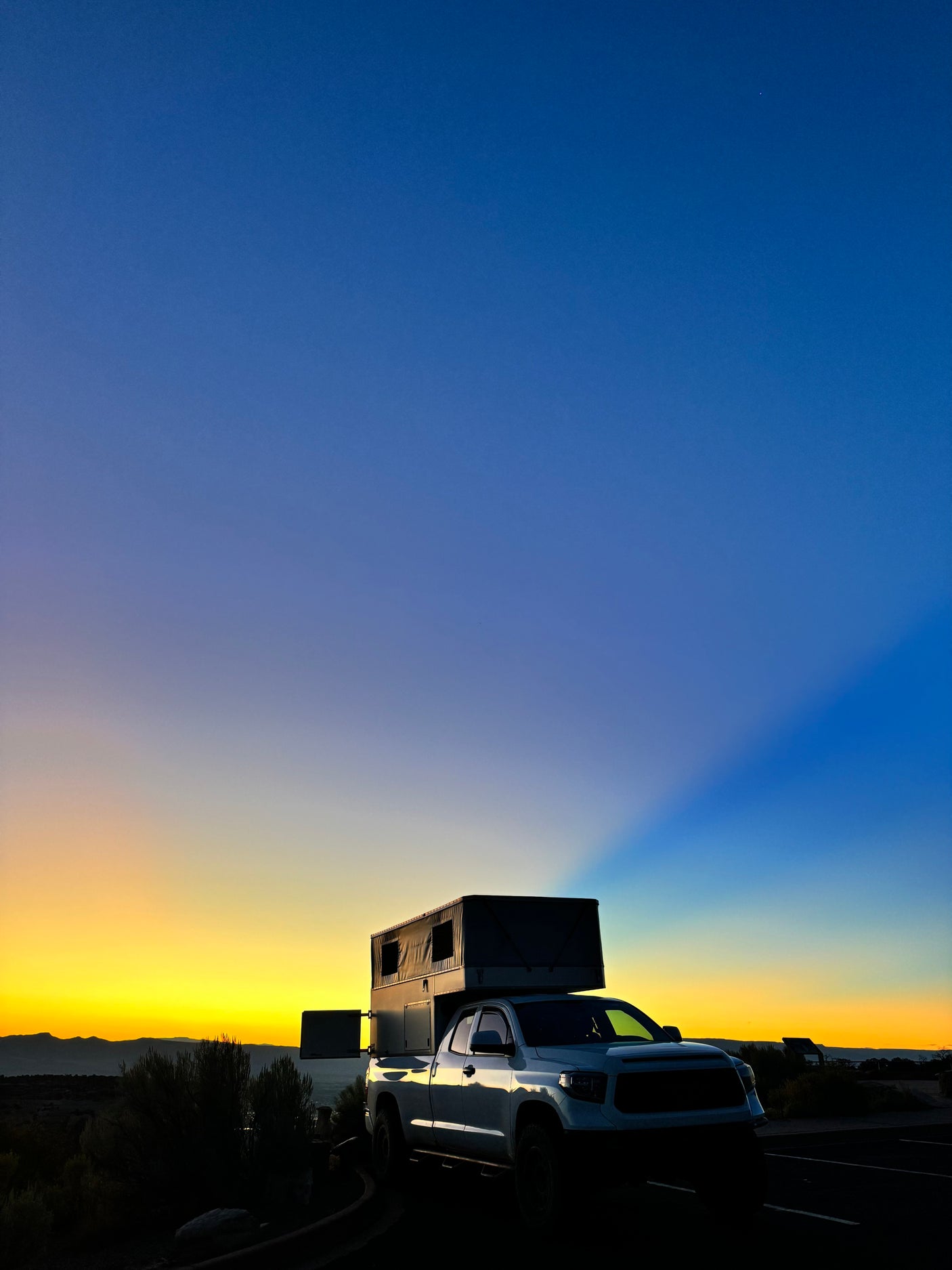 Witness epic sunsets from your RV rental! This truck camper overlooks a scenic landscape as the sky glows yellow & blue.