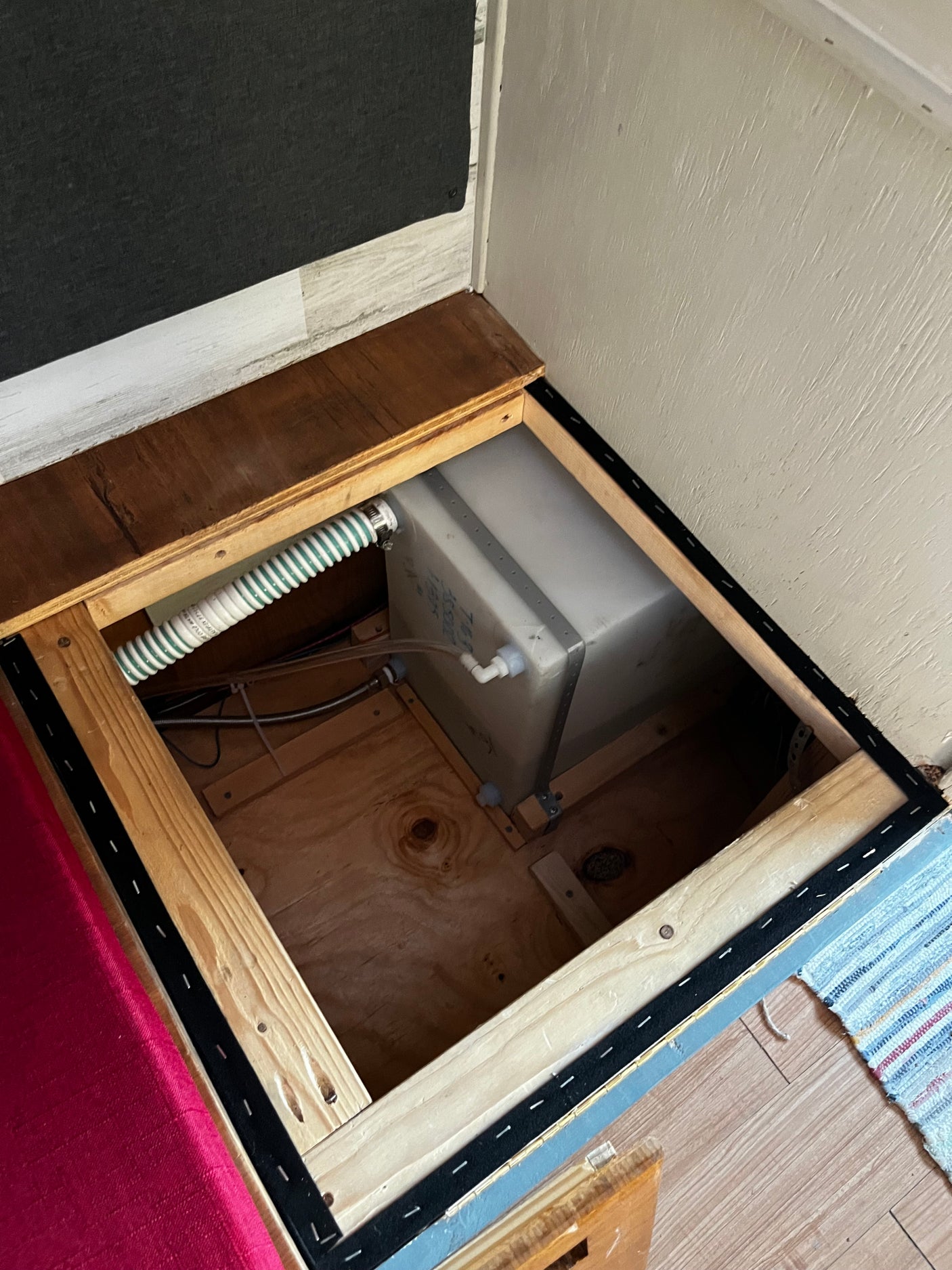 RV rental under-bed storage revealing a freshwater tank, plumbing, and wiring, neatly tucked away for compact living.