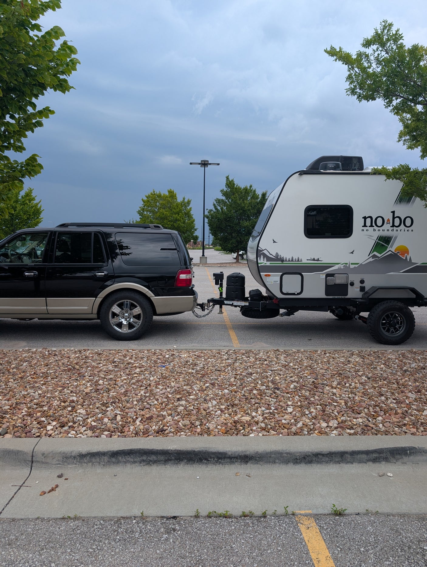 Black SUV towing a white and gray No Boundaries travel trailer, parked for an rv rental adventure. Great for camping trips.