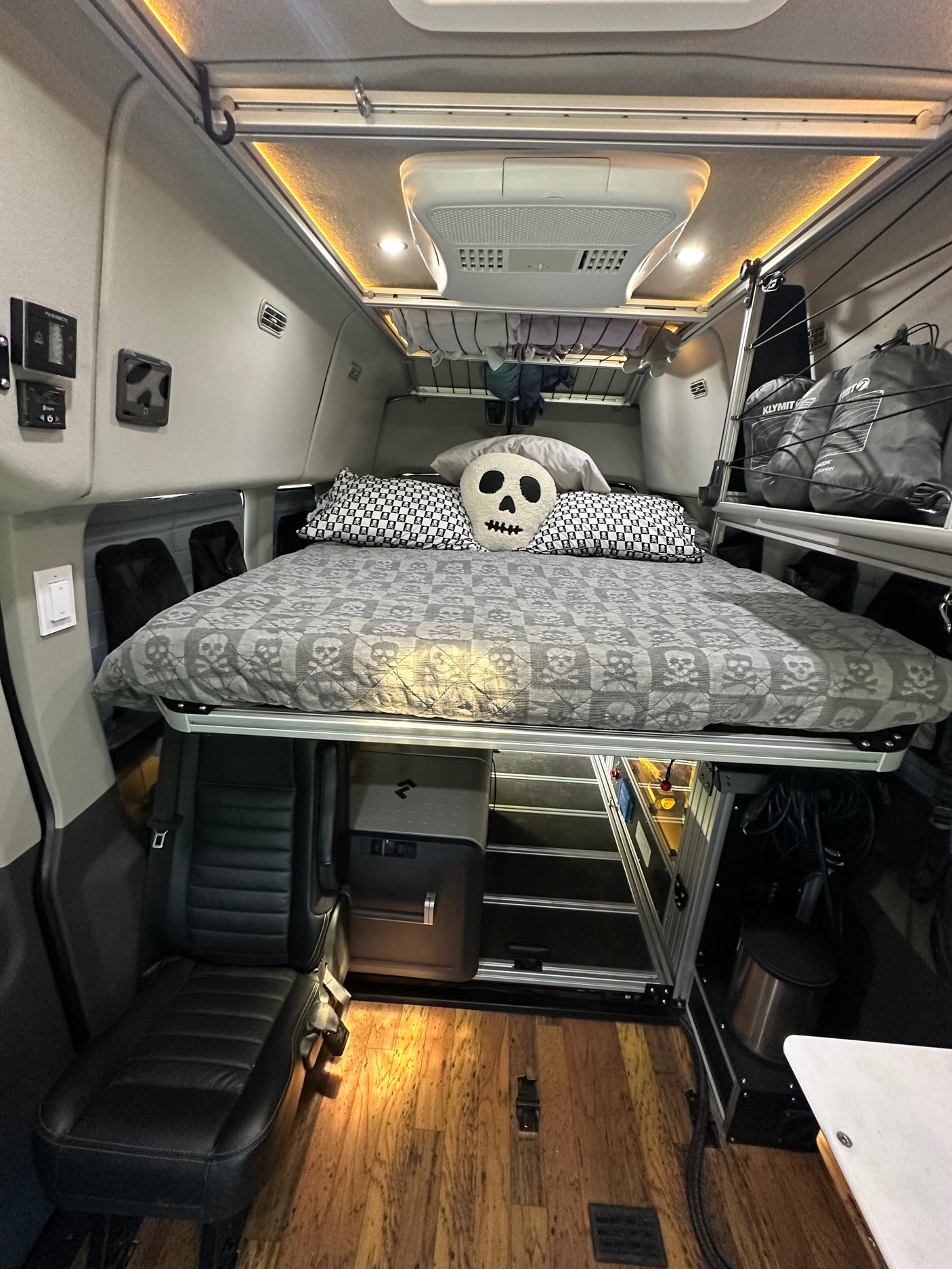 This modern rv rental camper van interior features a skull-themed raised bed, integrated fridge, seating, and overhead storage.