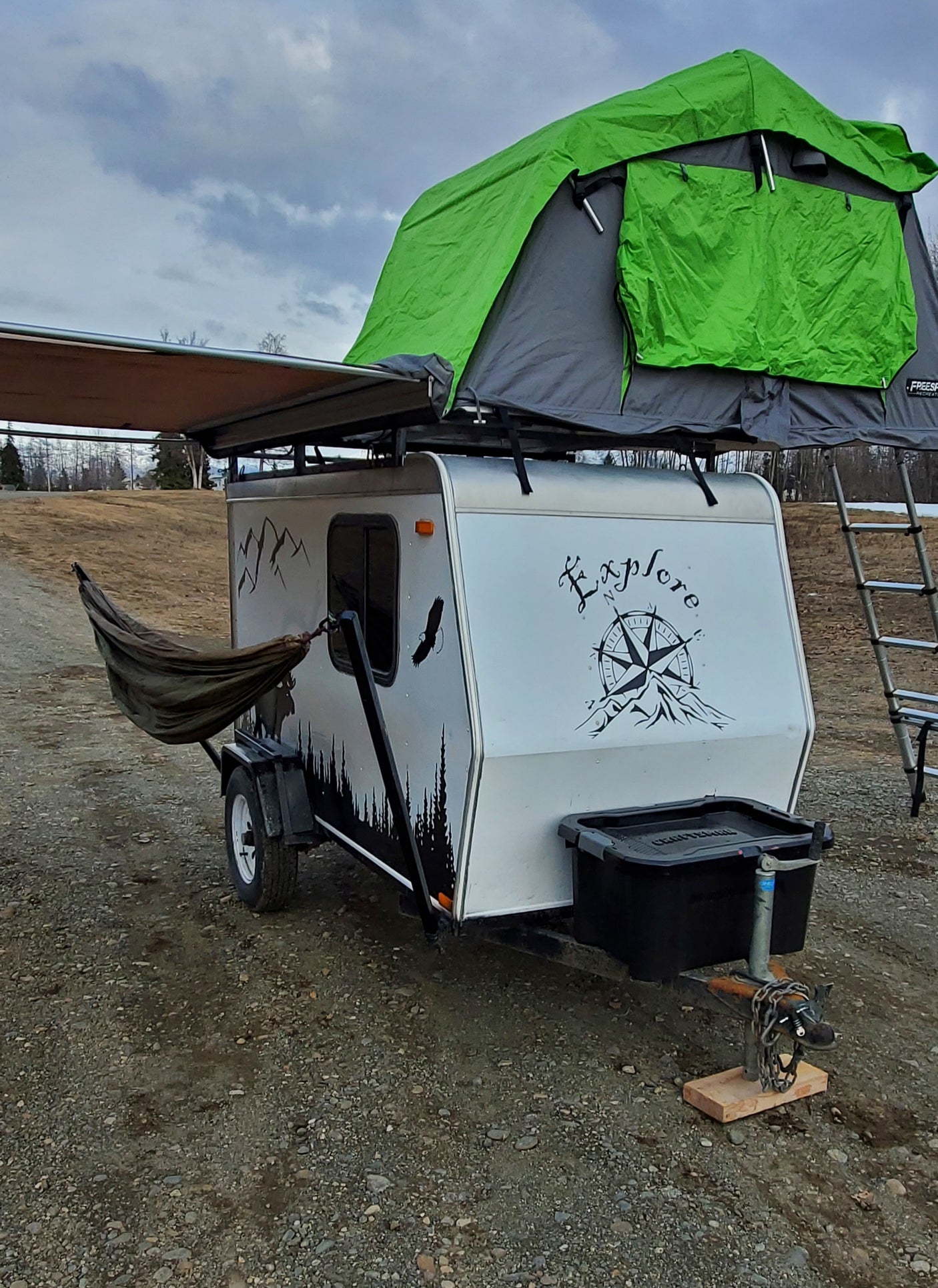 Compact RV rental: White teardrop camper with green rooftop tent, perfect for outdoor adventures.