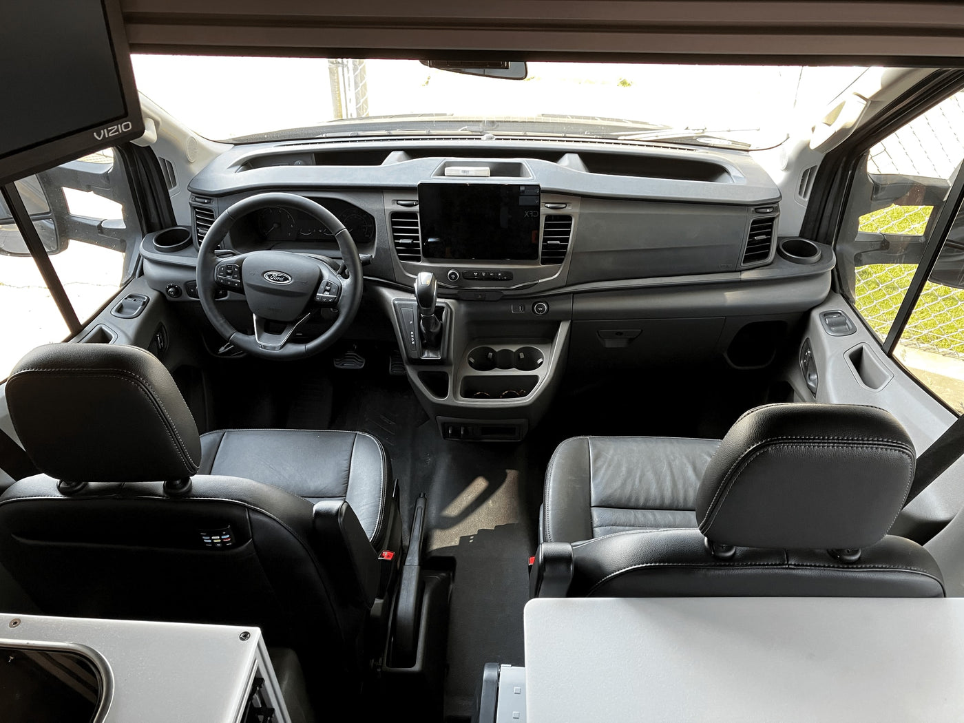Interior view of an RV rental's front cabin. Driver's seat, passenger seat, dashboard, and steering wheel are visible, plus a Vizio TV on the left. — photo 30
