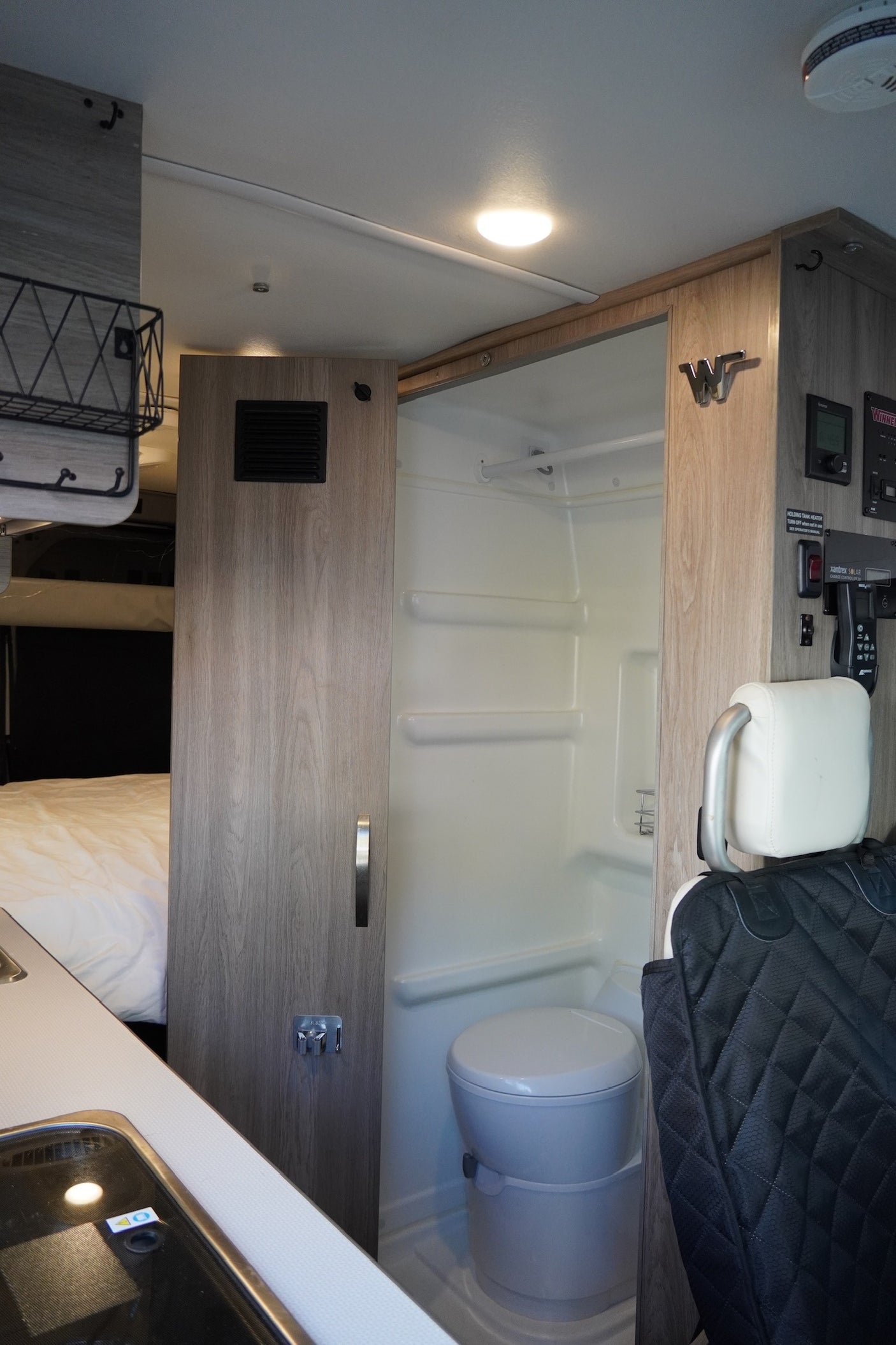 This RV rental interior showcases a compact wet bath with toilet and shower, alongside a bed and kitchen area.