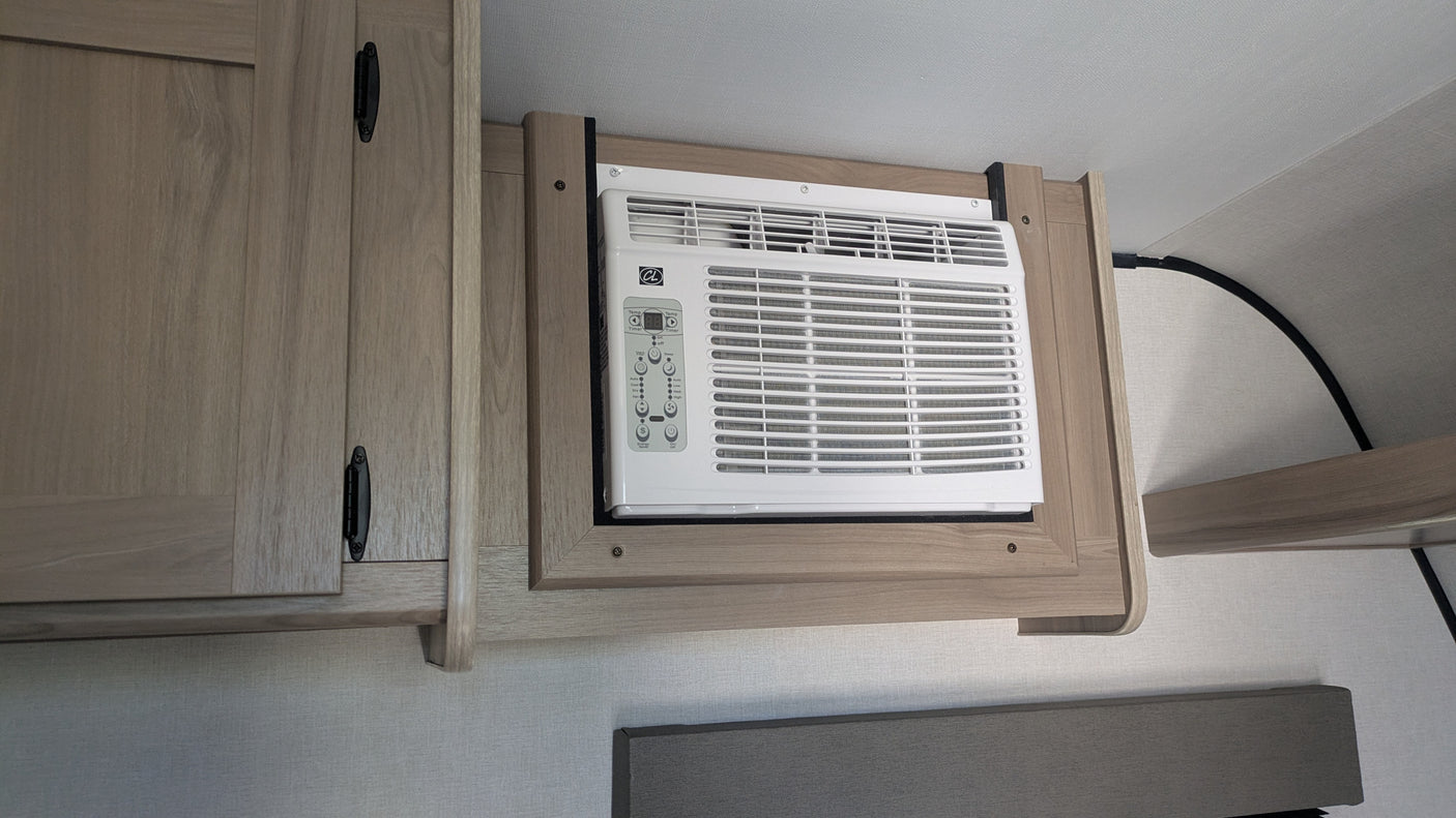 RV rental interior: A white window AC unit is integrated into light wood cabinetry, with controls visible, providing cooling.