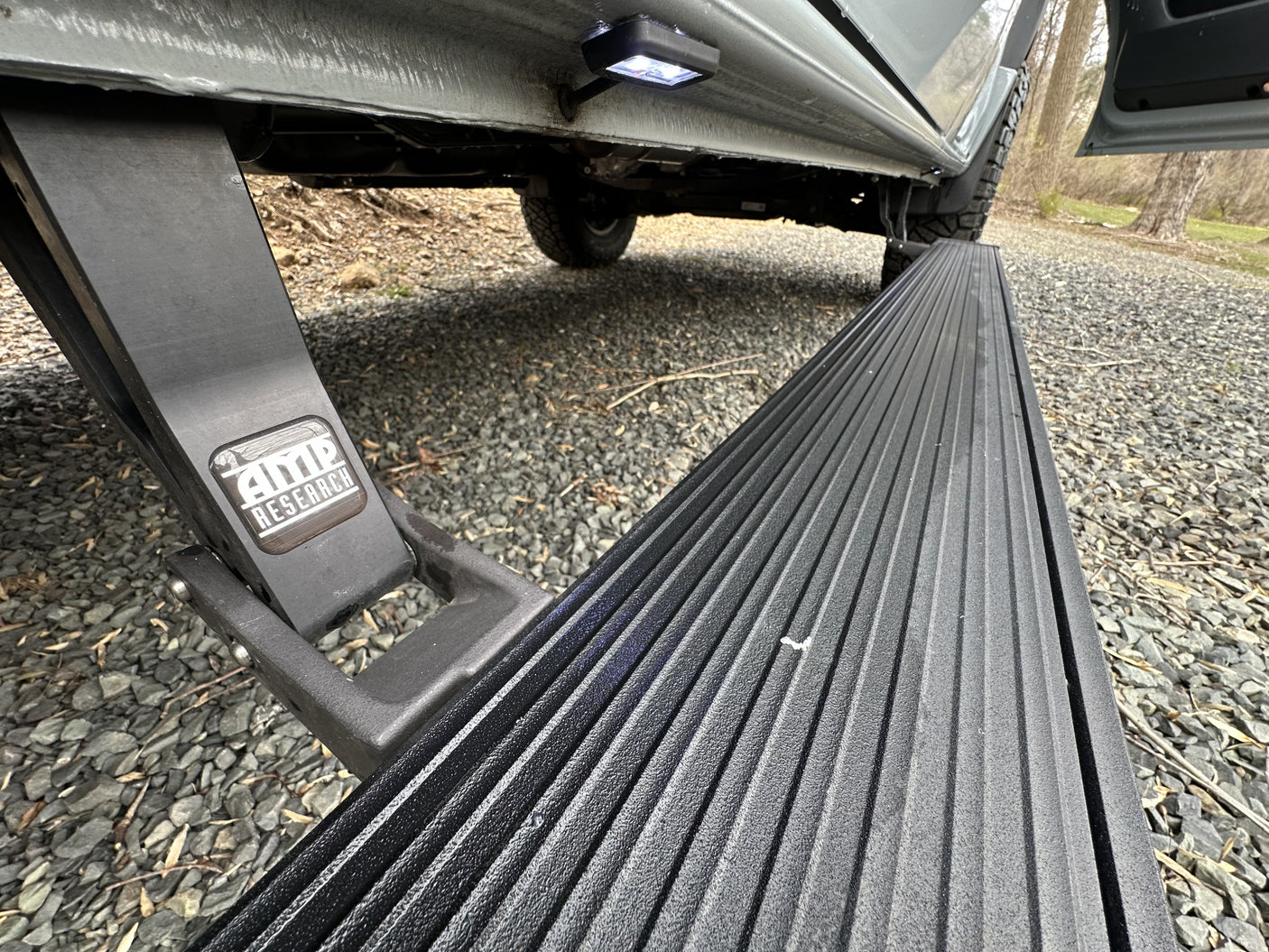 An RV rental features extended AMP Research power steps with LED lighting, making entry easy on this gravel surface.