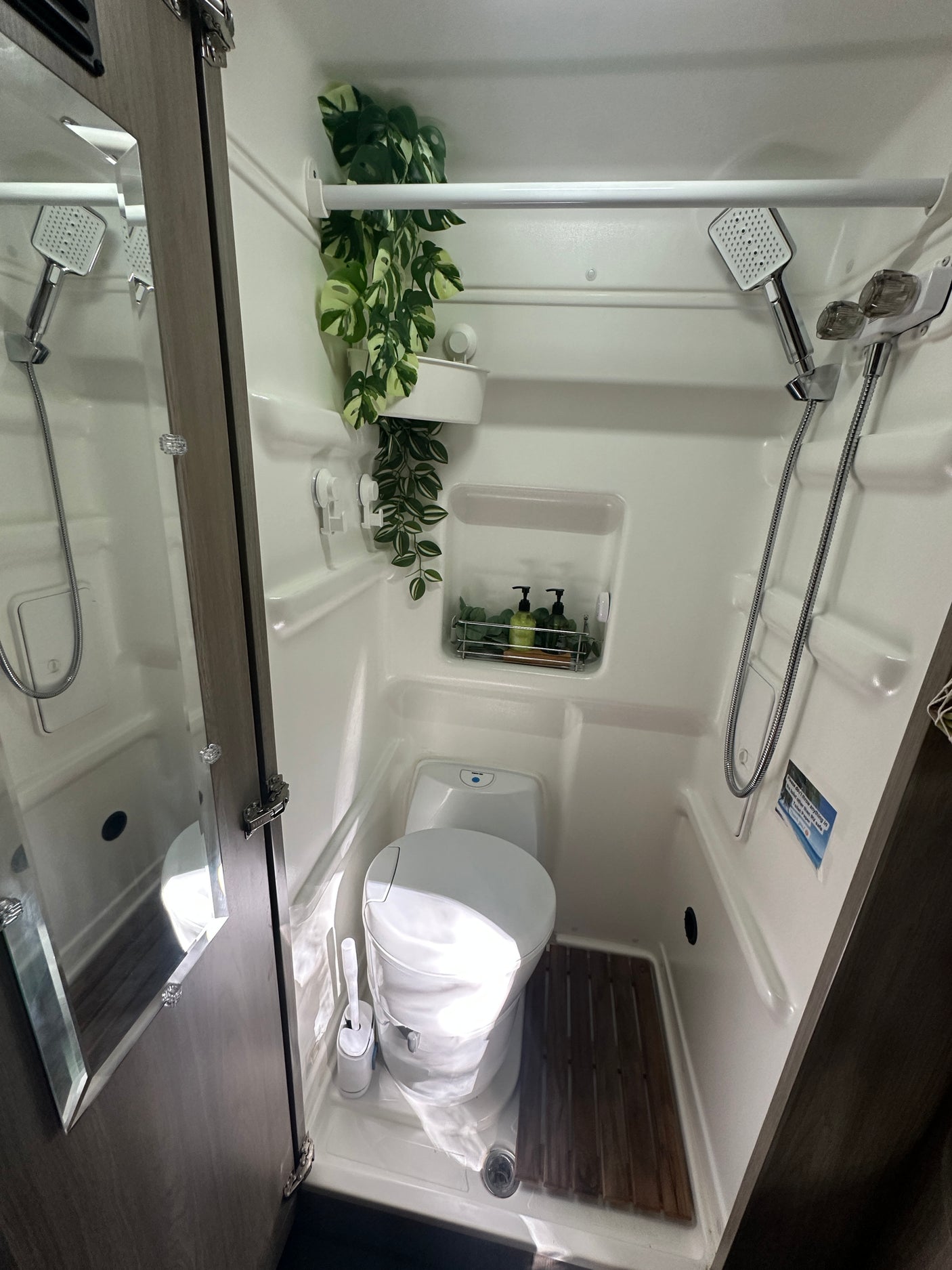 This RV rental wet bath features a compact toilet, shower, and practical shelving with toiletries, optimizing space for your journey.