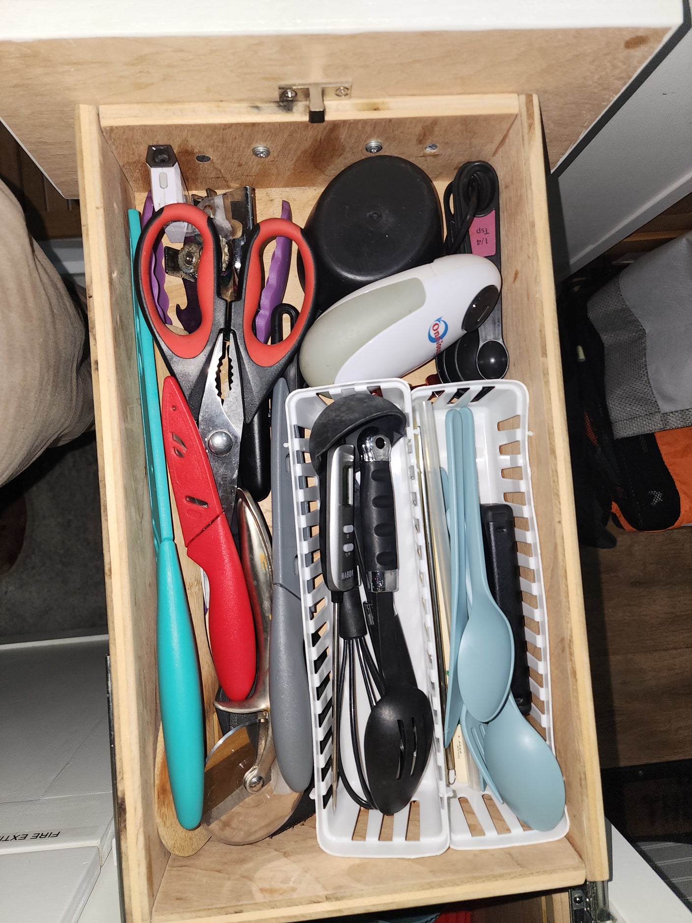 Inside an RV rental, a well-stocked kitchen drawer holds cooking utensils, knives, scissors, and a can opener, all organized.