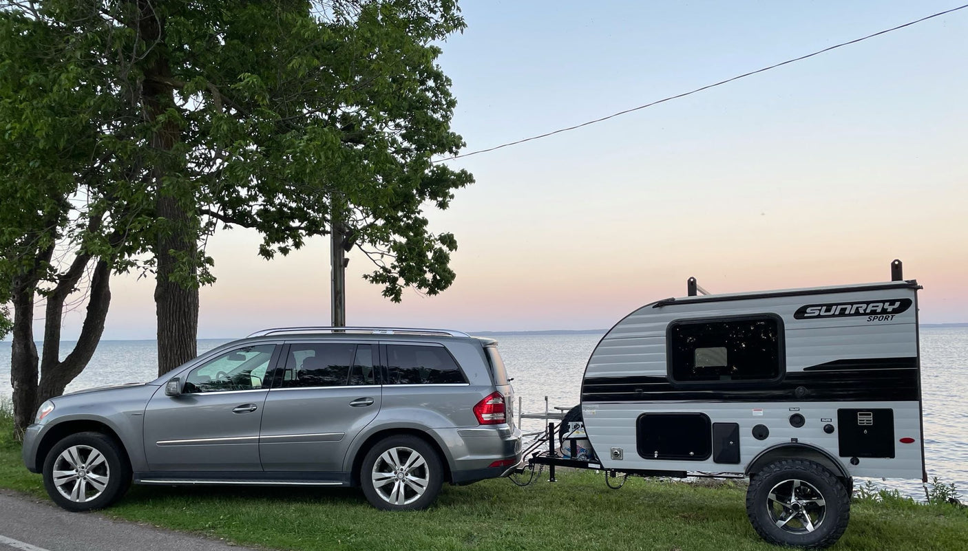 ready for adventure. Tow vehicle present.|Scenic RV rental trip: A gray SUV tows a Sunray Sport camper by a calm lake at sunset. Ideal for nature exploration.|This Sunray Sport travel trailer