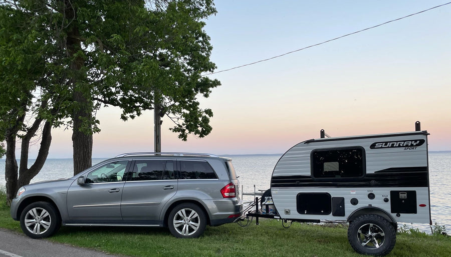 ready for adventure. Tow vehicle present.|Scenic RV rental trip: A gray SUV tows a Sunray Sport camper by a calm lake at sunset. Ideal for nature exploration.|This Sunray Sport travel trailer