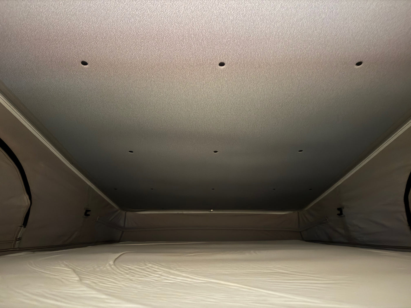 Pop-top RV rental interior: a comfy mattress and fabric walls, with small ceiling lights, ready for your adventure.