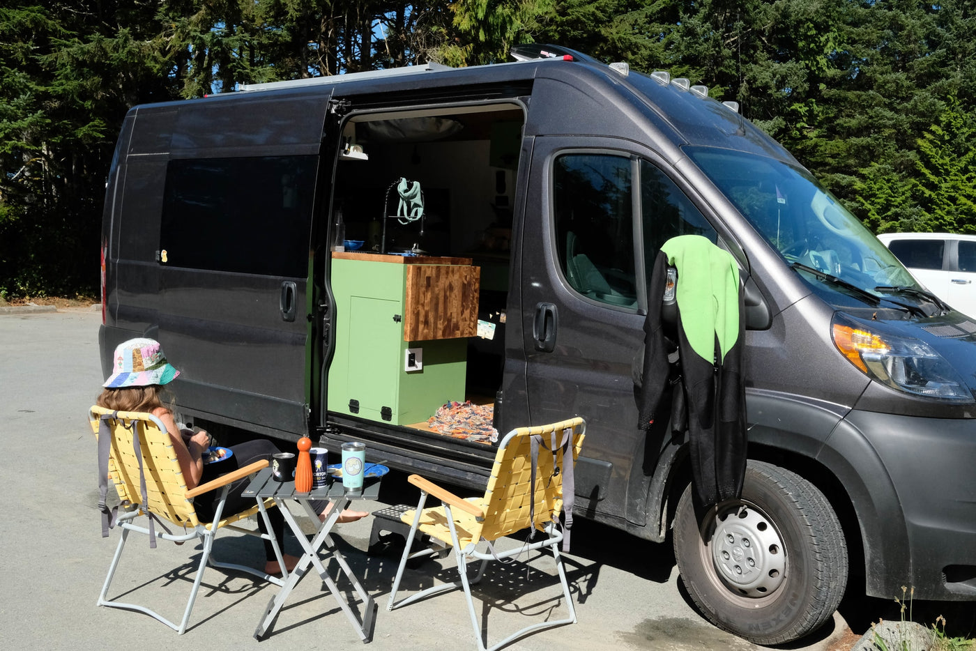 RV rental van life setup: Person enjoying a meal by their open camper van with wetsuit drying. — photo 3
