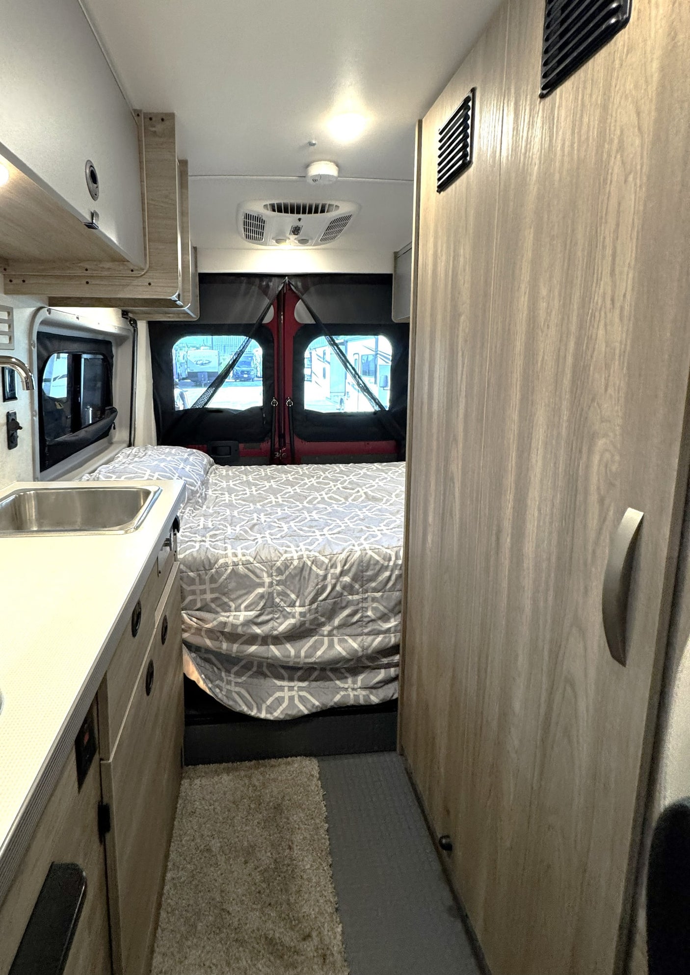 RV rental interior with a compact bedroom, kitchenette sink, and wooden storage cabinetry, ideal for travelers.