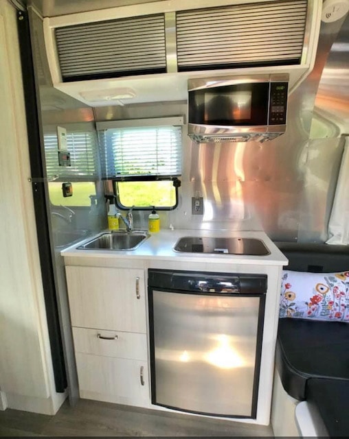 Modern RV rental kitchen with stainless steel appliances: sink, cooktop, microwave, fridge, and overhead storage. Ready for adventure!
