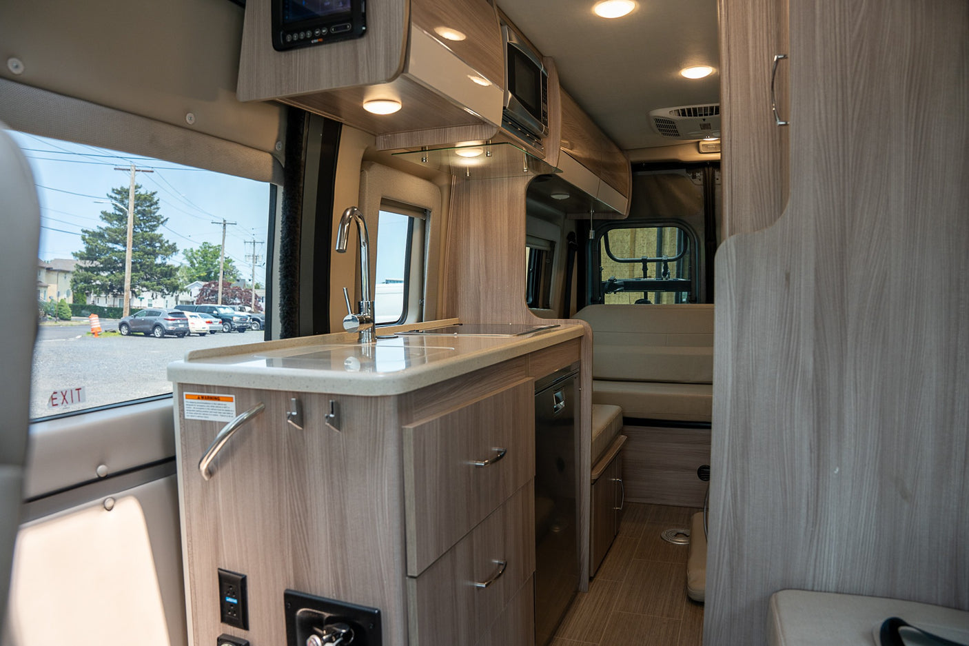 Modern RV rental interior with a light wood kitchen featuring a sink, microwave, and adjacent seating area.