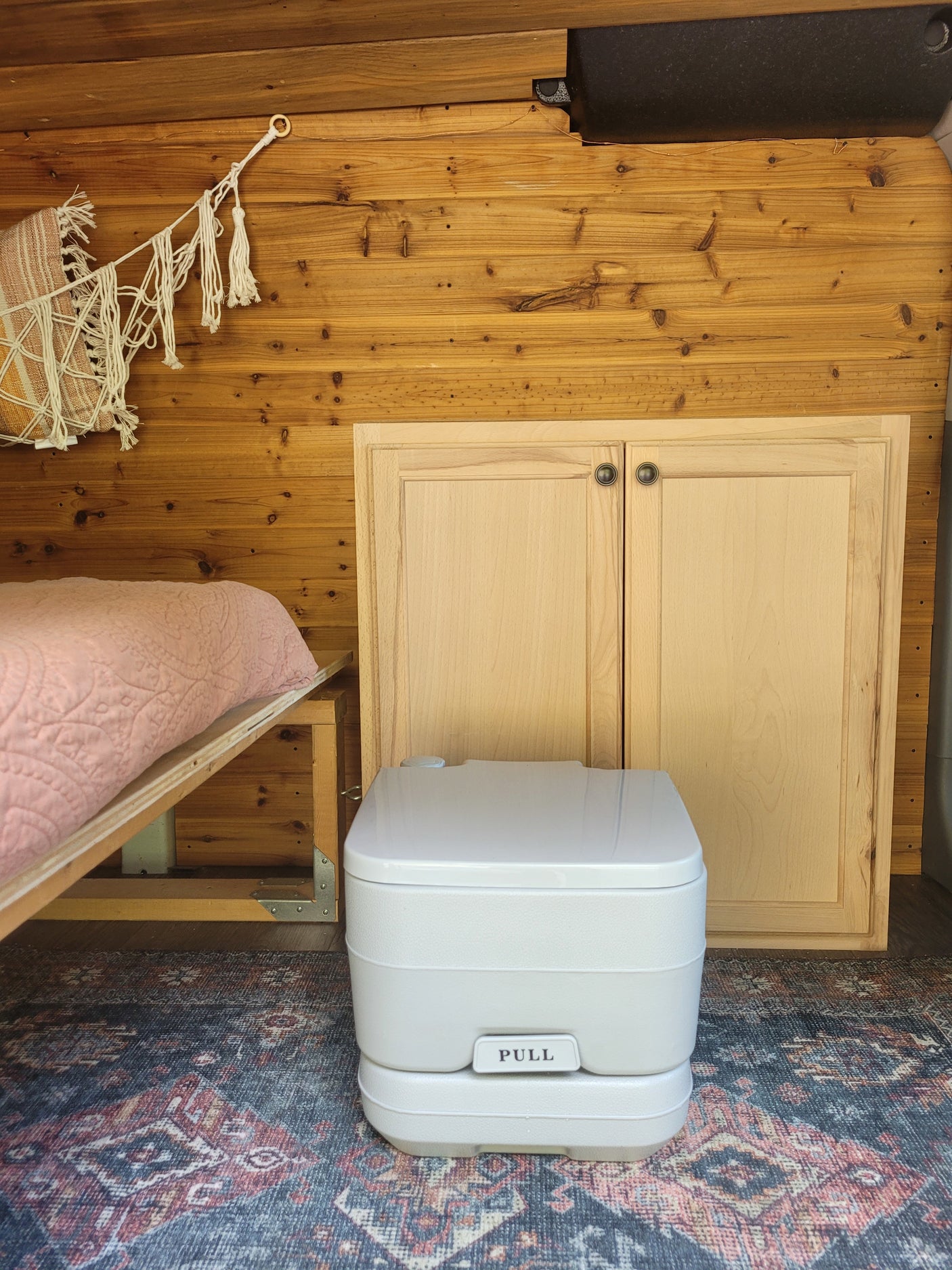 RV rental interior: cozy bed, wooden walls, and essential portable toilet for comfortable van life adventures.