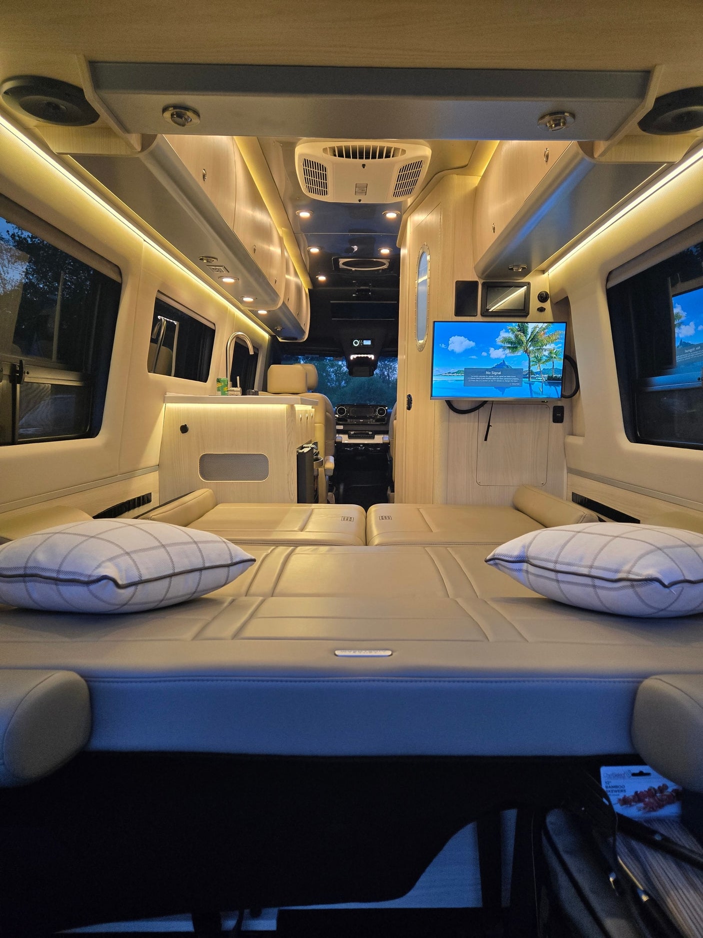 Spacious RV rental interior featuring comfortable beds, a kitchenette, and TV, warmly lit. Perfect for cozy road trips.