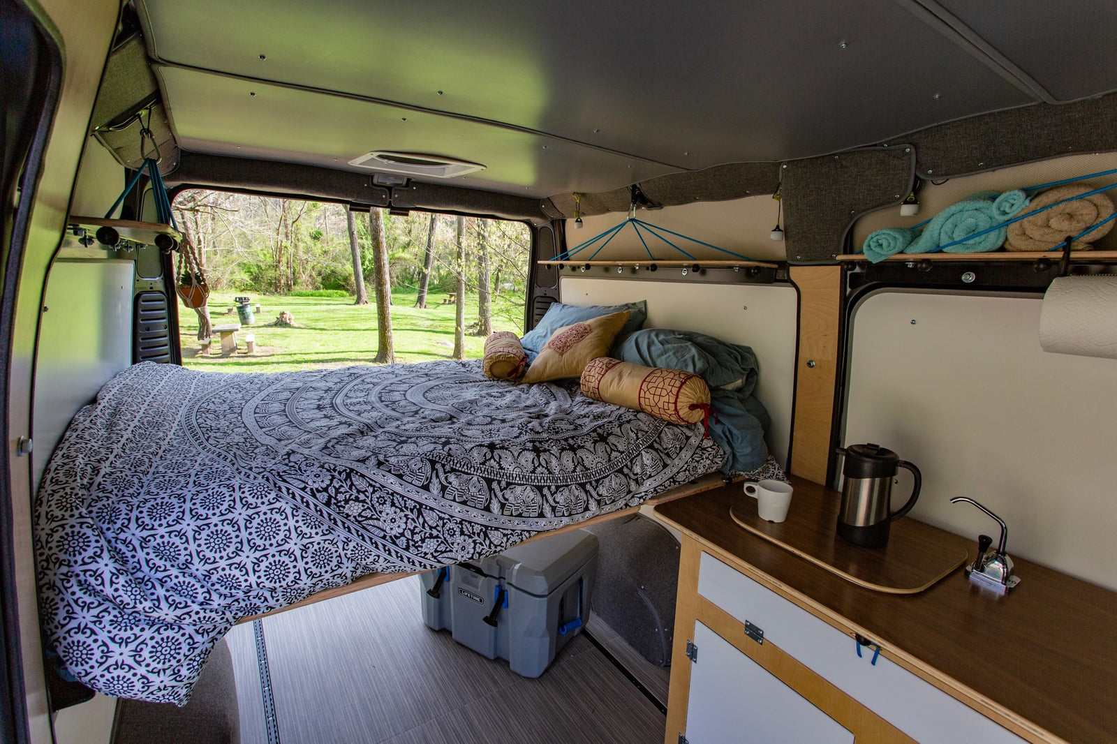 Inside a cozy RV rental van: a comfy bed with patterned cover