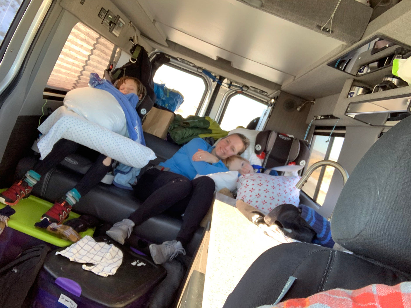 Inside an RV rental, a family of three enjoys a cozy rest on the vehicle's bench seating during their travels.