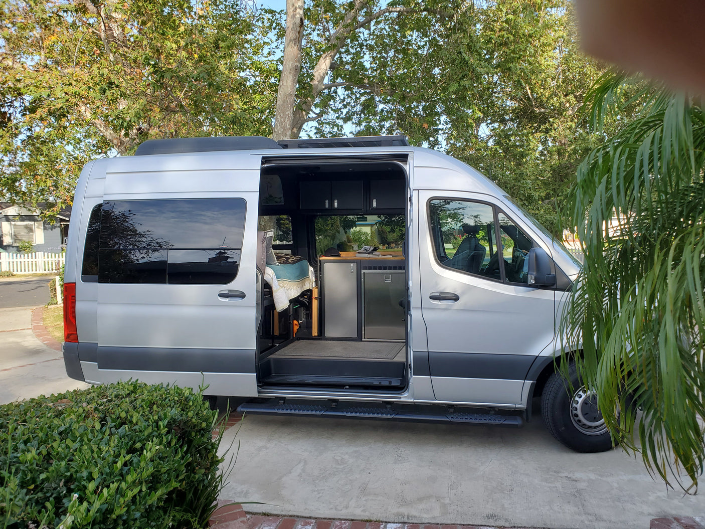 Explore a modern rv rental camper van, featuring an open side door, custom bed, and kitchen amenities.