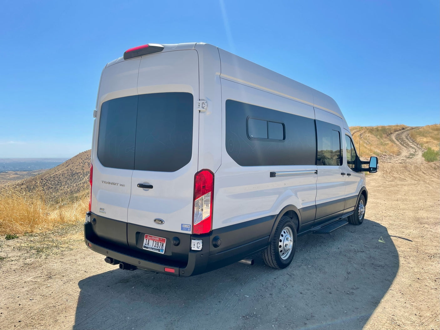 White Ford Transit RV rental van parked on a dirt trail, ready for outdoor adventure in a dry, hilly landscape.