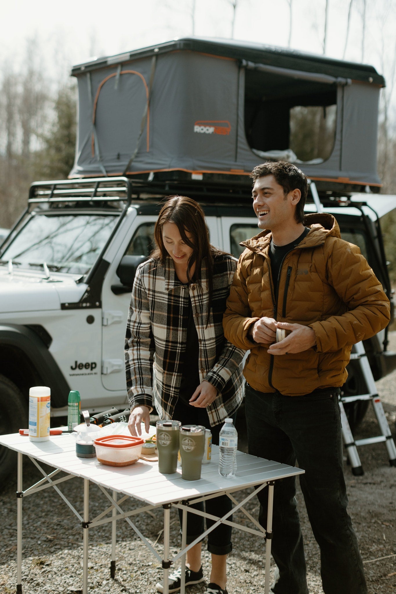 Campers prep food on a portable table beside their Jeep and rooftop tent, an ideal setup for a compact **RV rental** trip.