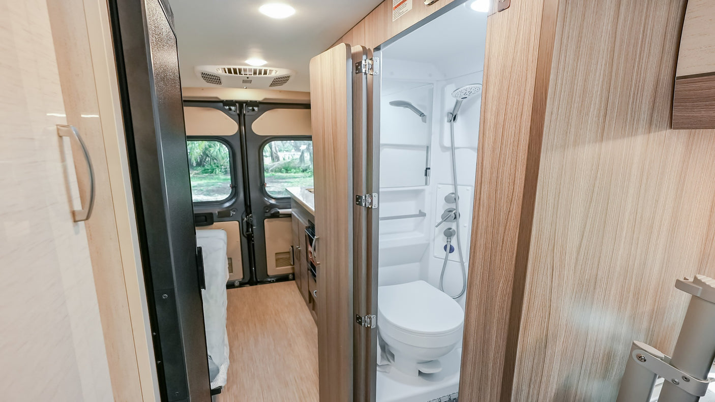 Compact RV rental interior: Bathroom with shower & toilet, leading to kitchen & rear view. Perfect for adventures!