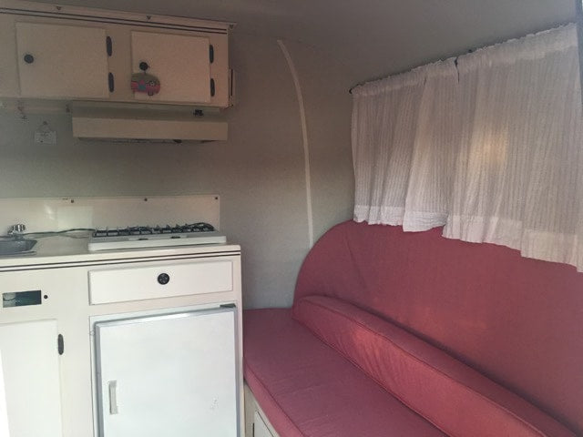 RV rental interior: compact kitchen (stove, sink, fridge) & red cushioned bench for travel comfort. — photo 6