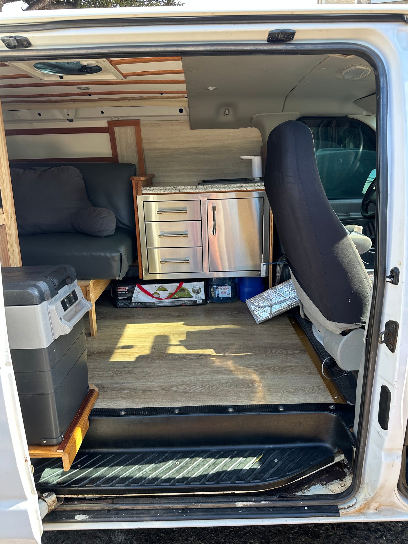 RV rental camper van interior. Features a compact kitchenette, convertible seating/bed, and portable fridge for travel.