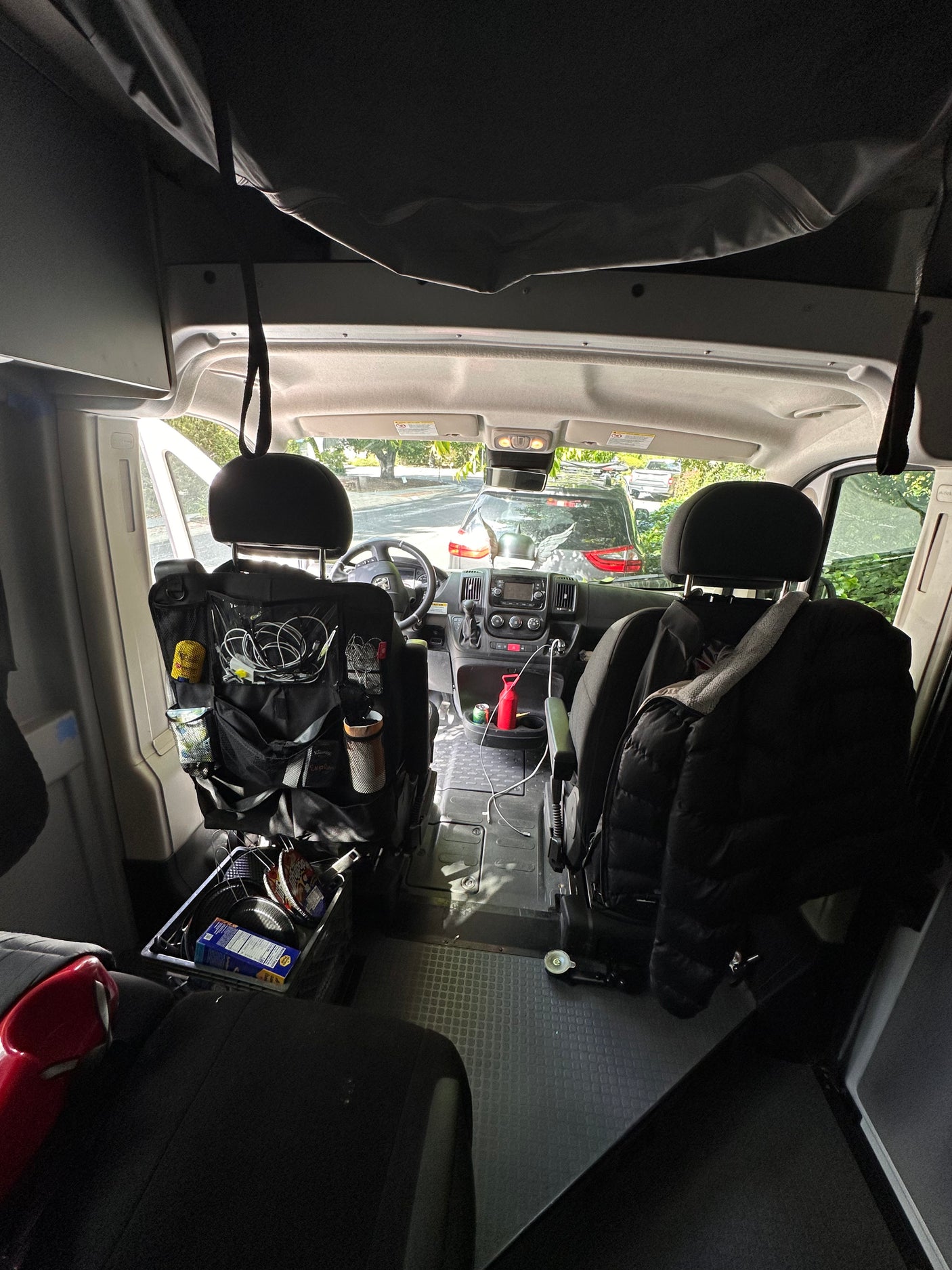 View into the front of an rv rental van, showcasing driver's area, passenger seat, and behind-seat organizers.
