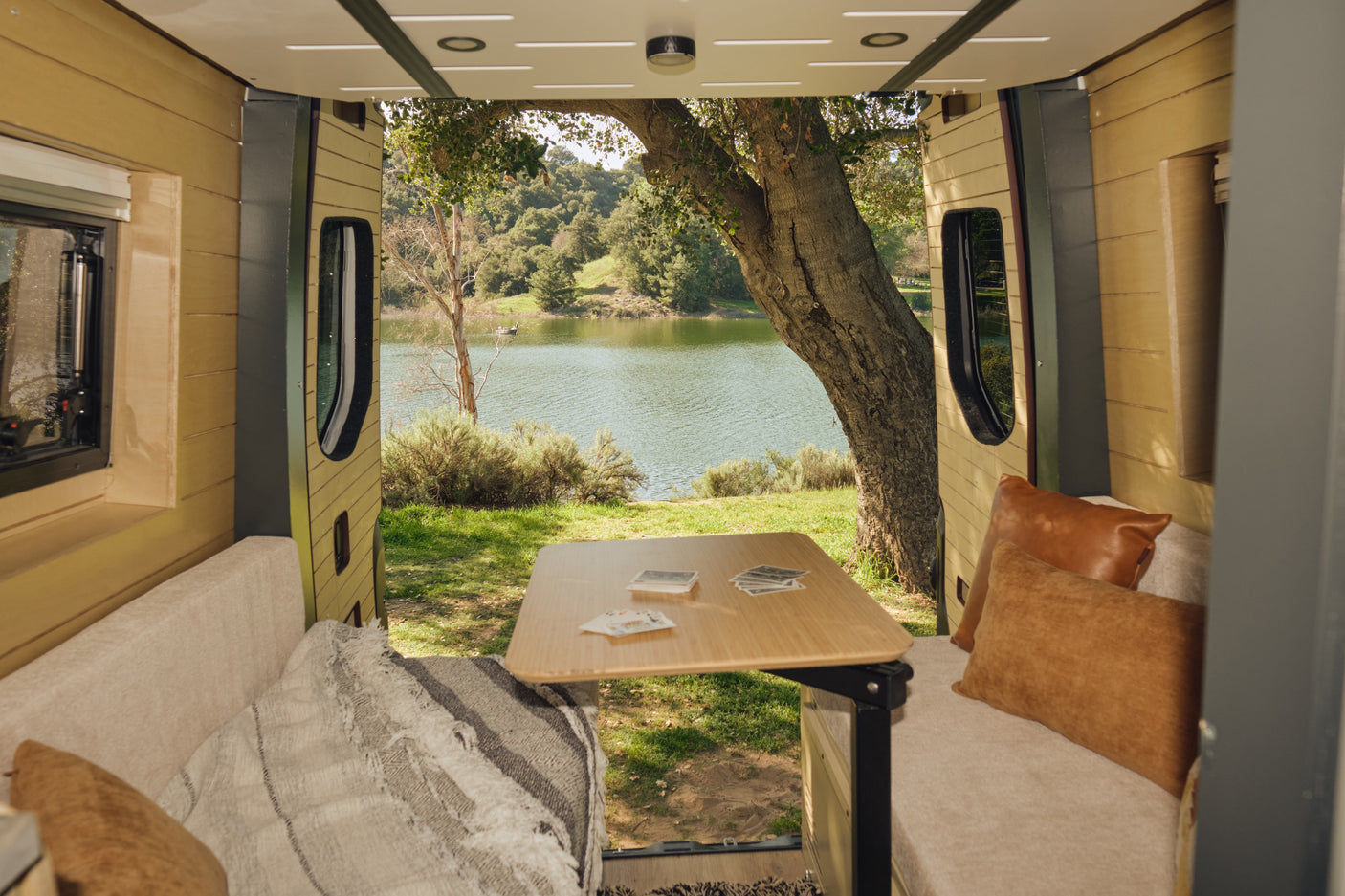 Enjoy this cozy rv rental interior with open doors, revealing a serene lake view, lush trees, and cards on the table.