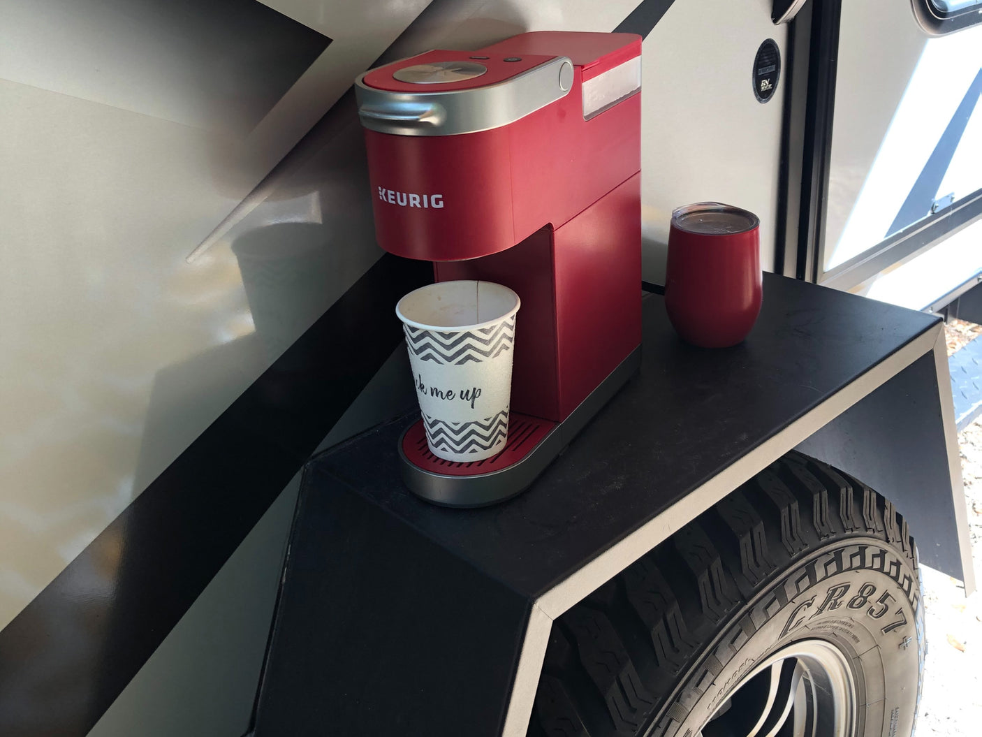 Red Keurig coffee maker and travel cups on an outdoor shelf of an RV rental, offering roadside convenience.