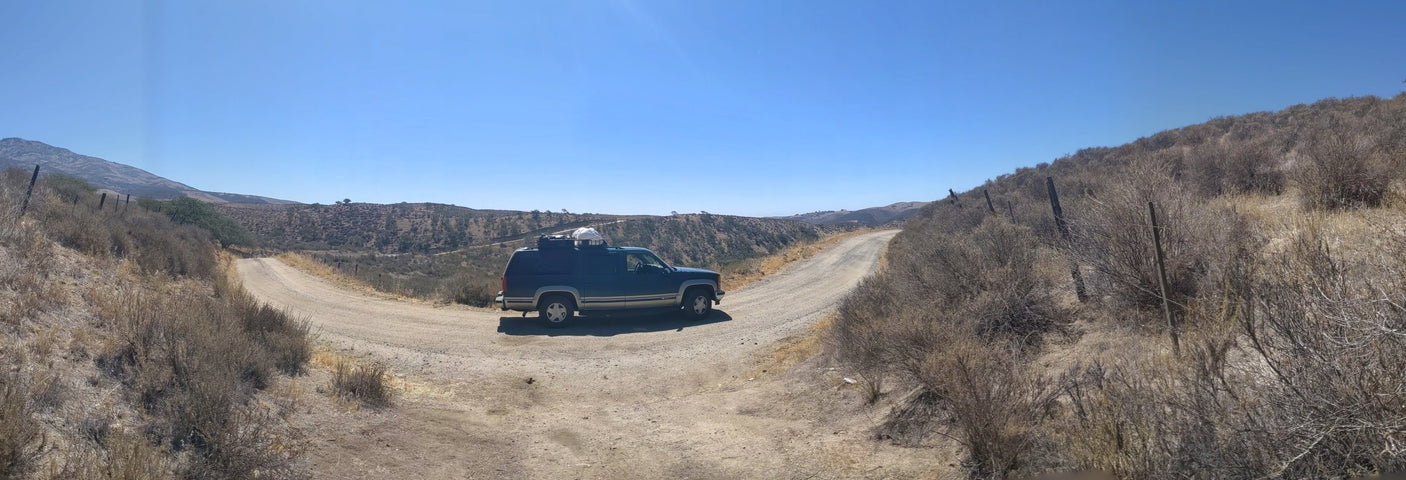 Dark SUV, ideal for an RV rental adventure, at a dirt road fork in dry hills.