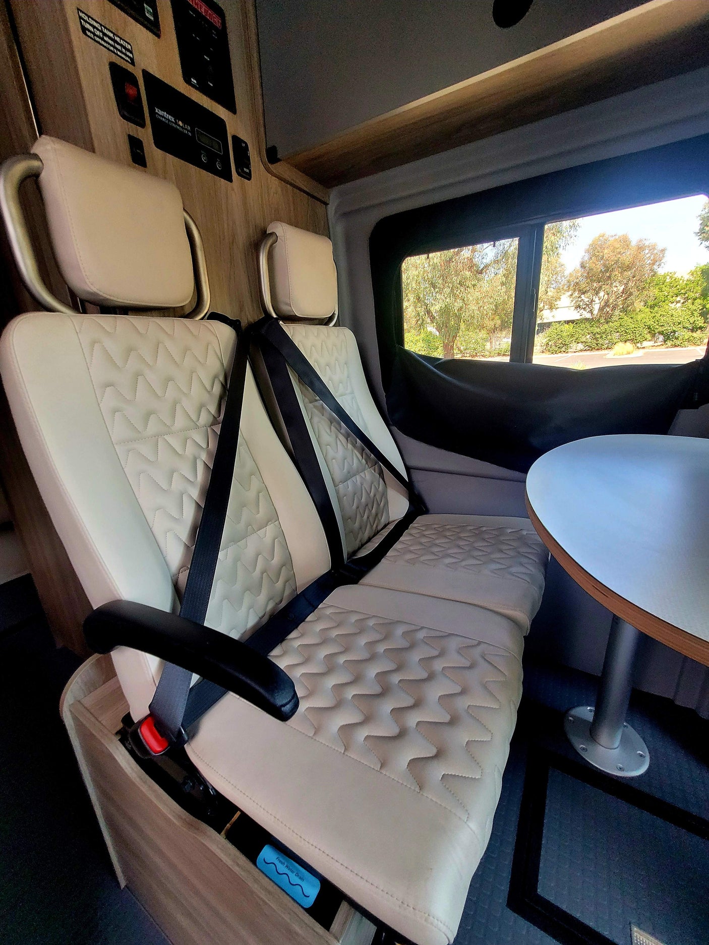 An RV rental's cozy interior, featuring light quilted seats with seatbelts, a small table, and useful system controls for your trip.