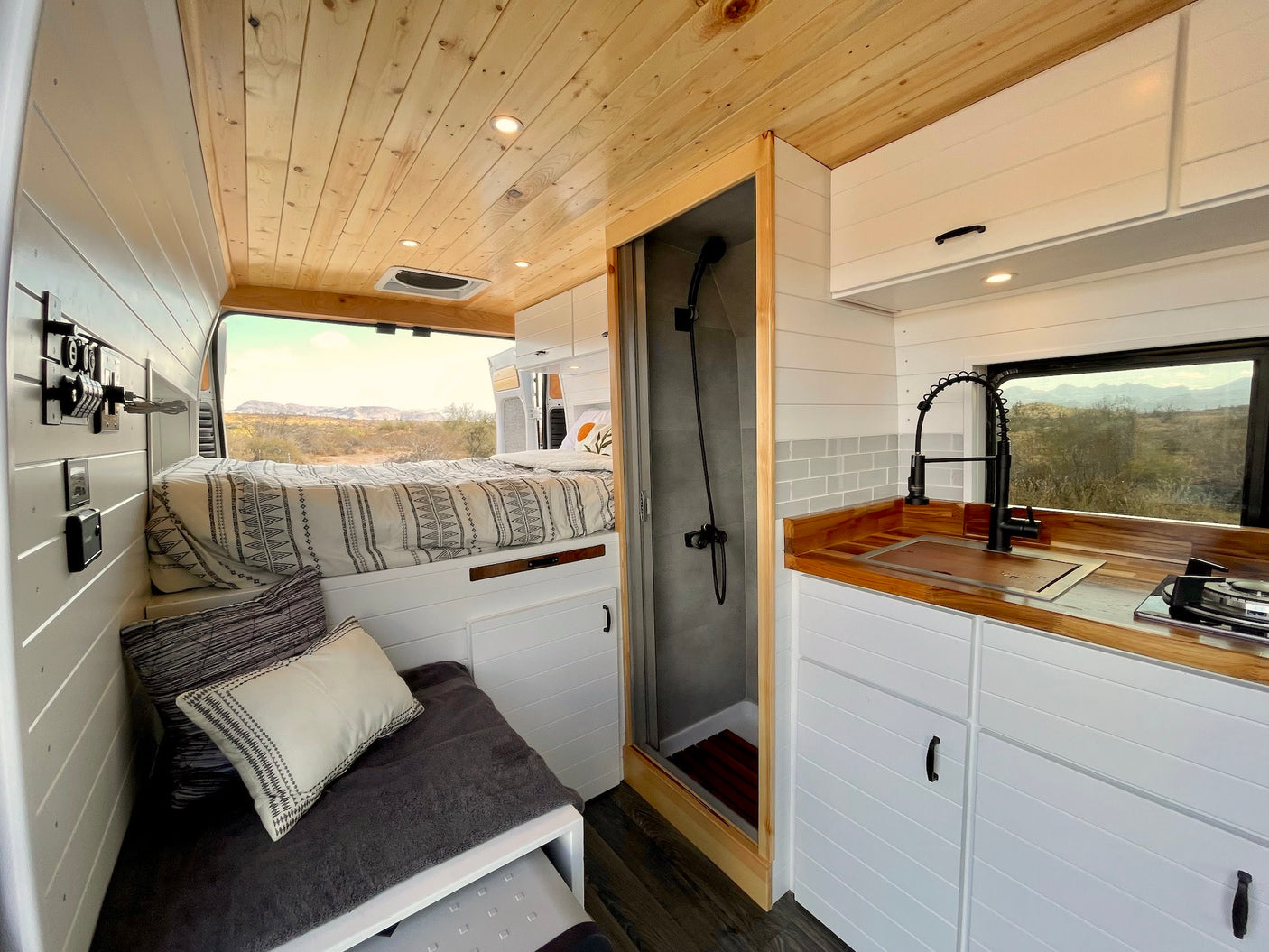Bright rv rental interior: bed, compact kitchen, and shower unit in a modern custom van, perfect for travel.