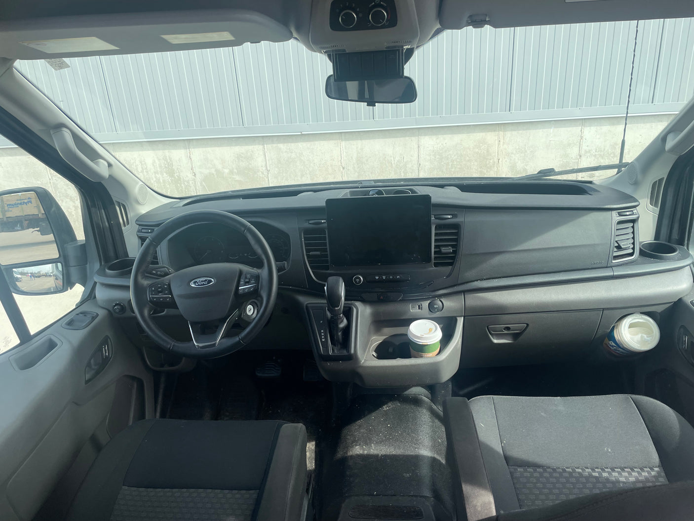 RV rental van interior: Driver's view of a modern Ford dashboard with an infotainment screen, steering wheel, and coffee cup.