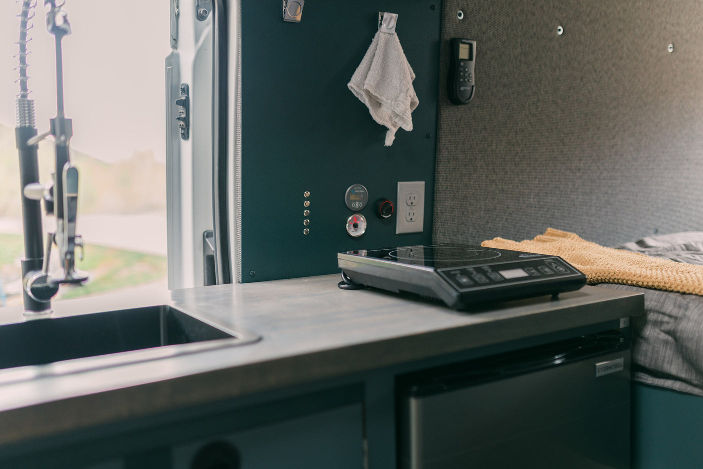 RV rental interior: compact kitchen with sink, induction cooktop, fridge, and control panel for comfortable mobile living.