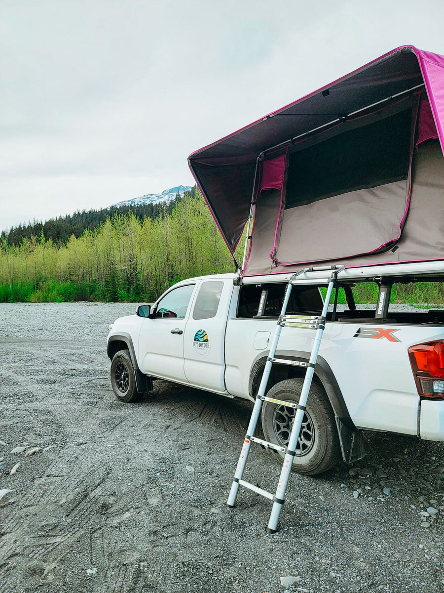 ready for a mountain adventure. Your perfect RV rental for exploring the outdoors!|White pickup with a vibrant pink roof-top tent ready for an RV rental adventure