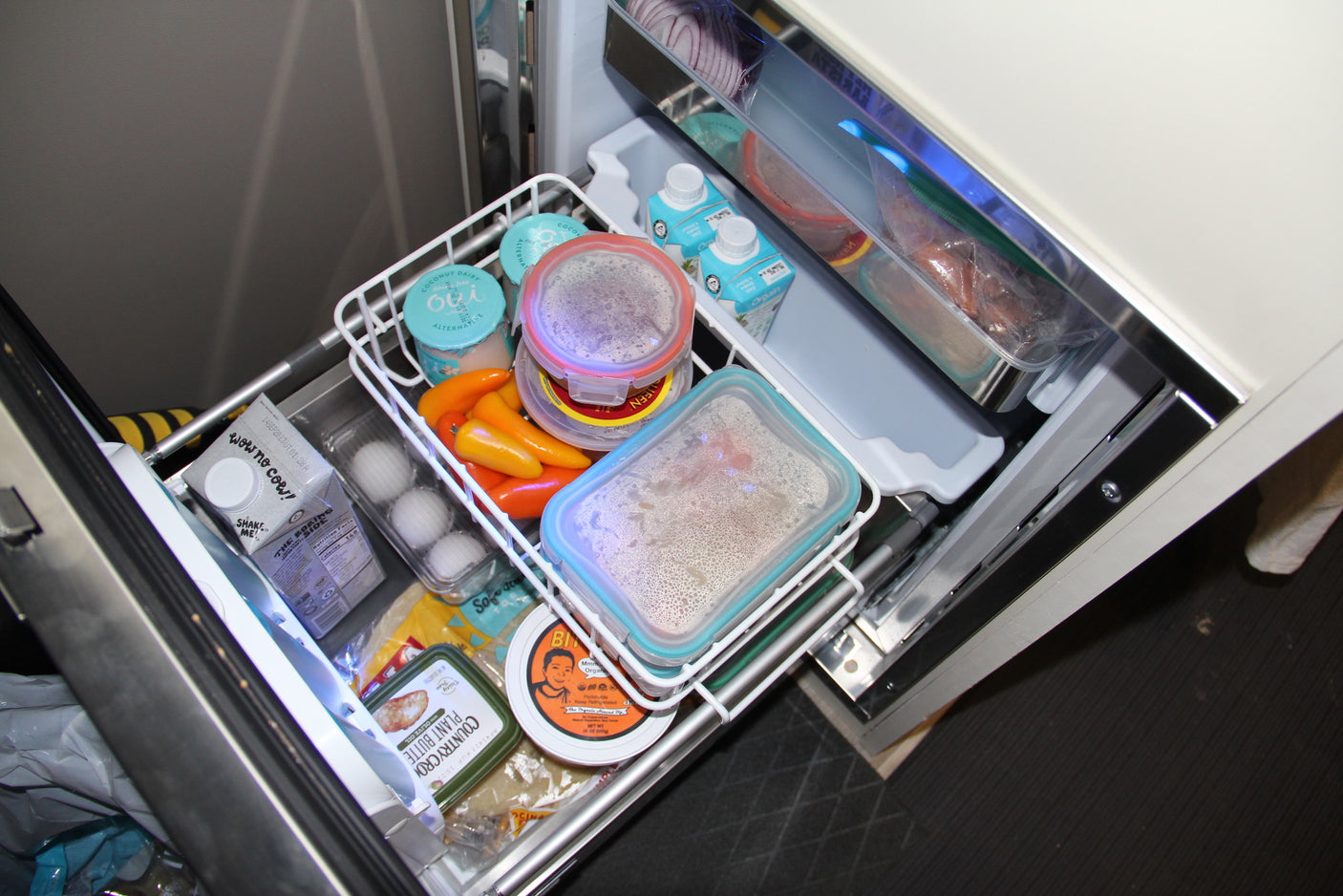 Compact RV rental fridge drawer neatly organized with dairy-free yogurt, plant-based butter, milk, and prepared meals.