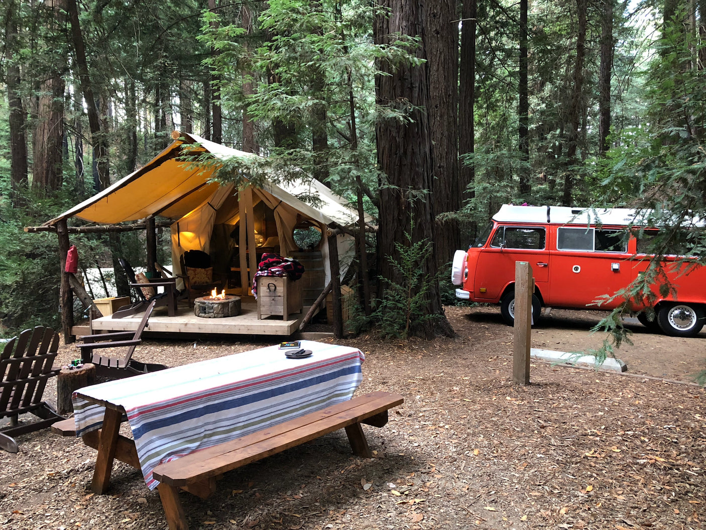 RV rental: Vintage red camper van, glamping tent, and fire pit offer a unique outdoor stay amidst towering redwoods.