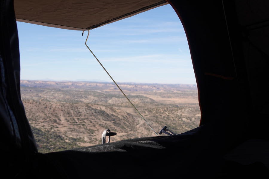 Scenic RV rental view from inside: a vast desert landscape with mesas under a blue sky, seen through a tent window.