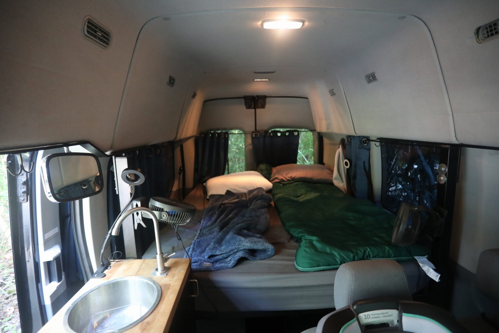 parked on a sunny dirt path in the woods.|Black Wandervans campervan RV rental parked in woods with open side door