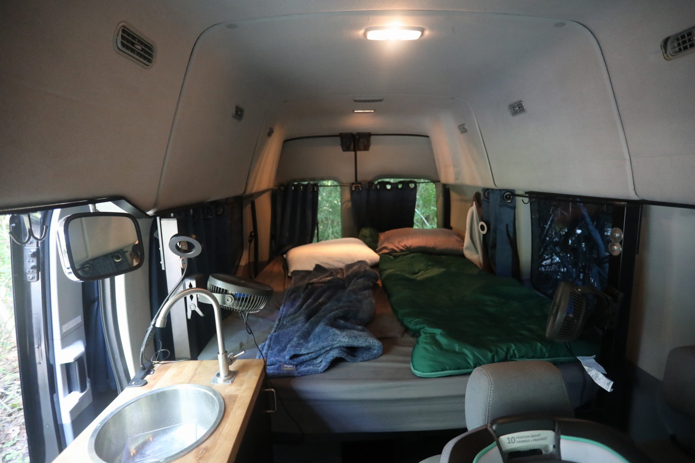 parked on a sunny dirt path in the woods.|Black Wandervans campervan RV rental parked in woods with open side door
