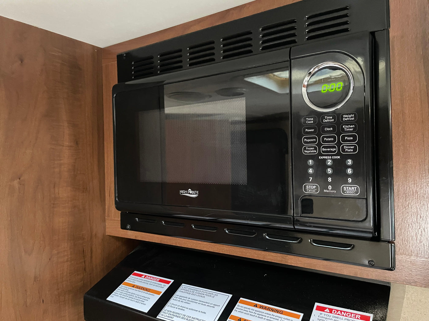 Built-in High Pointe microwave in an RV rental kitchen. The black microwave shows 0:00 on its display, surrounded by wood cabinetry. — photo 12