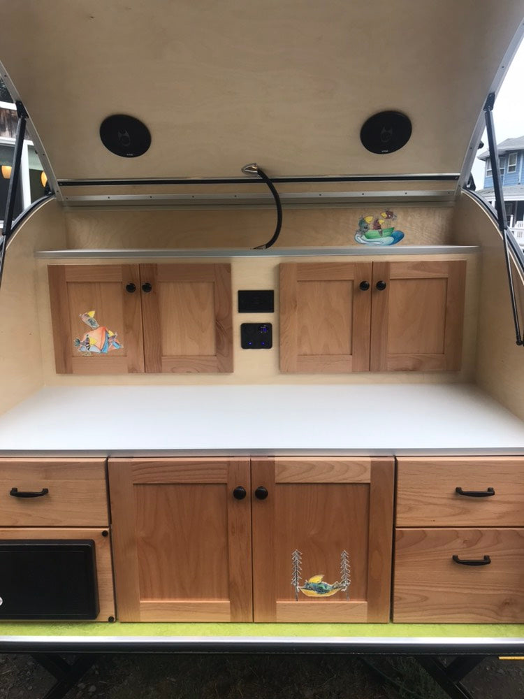 Compact RV rental galley with wooden cabinets, countertop, and fun decals, perfect for travel.