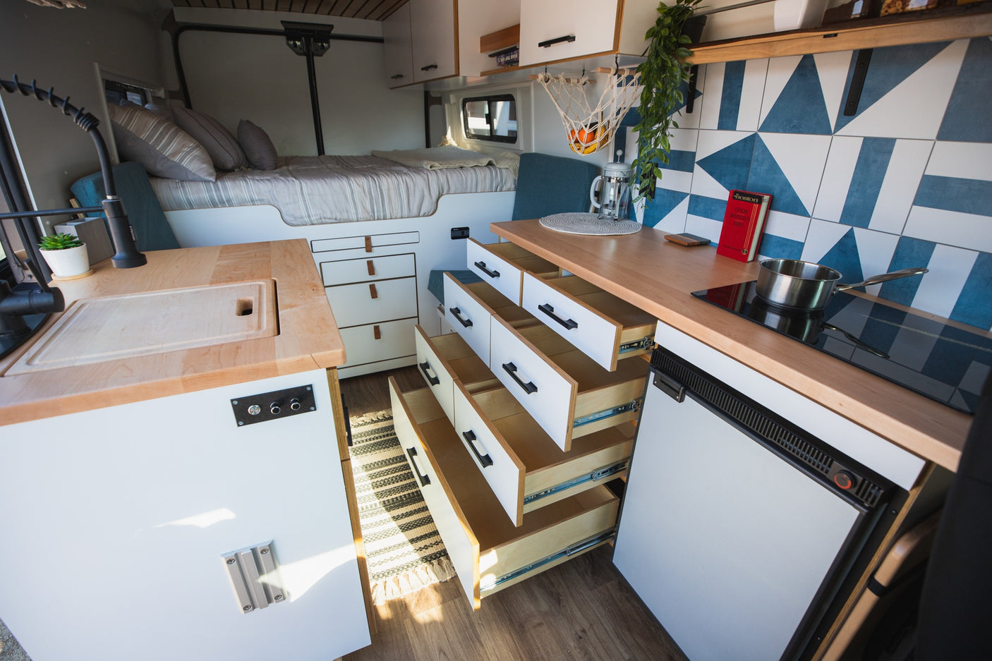 RV rental interior showing a bed, kitchen with sink & induction cooktop, plus many open storage drawers. Organized van life.