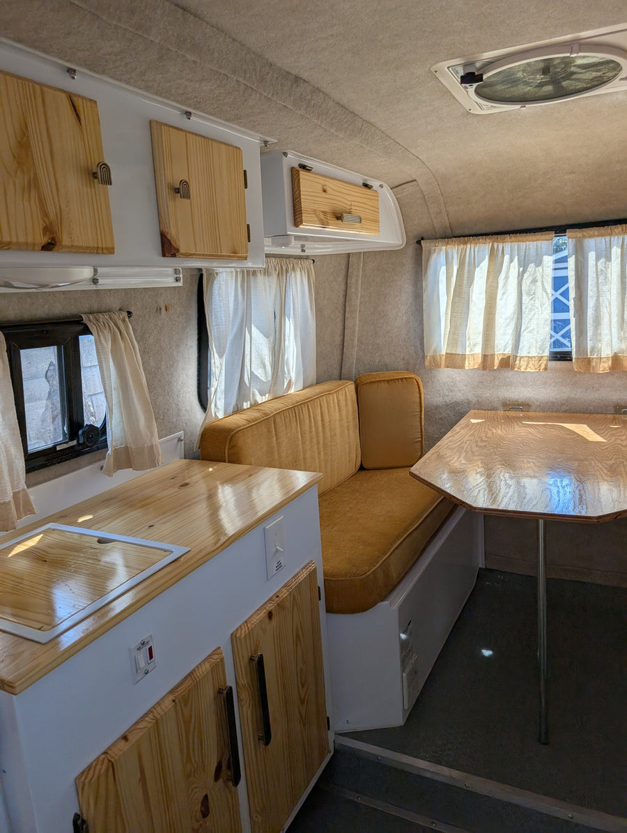 Step into this cozy RV rental's renovated interior, showcasing wooden cabinets, mustard cushions, and a compact kitchen.