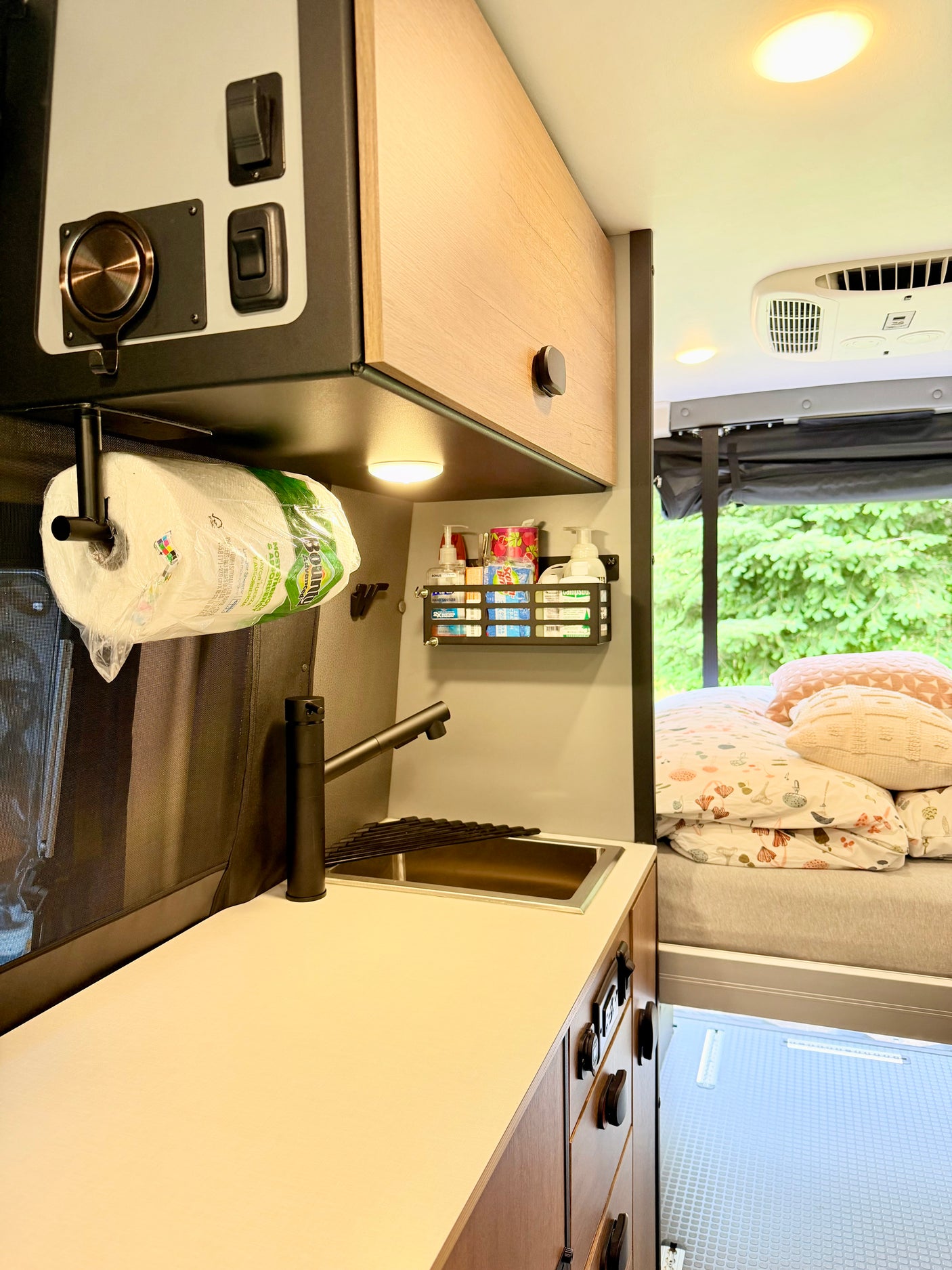 RV rental interior featuring a compact kitchenette with sink, faucet, paper towels, and storage, plus a cozy bed area.