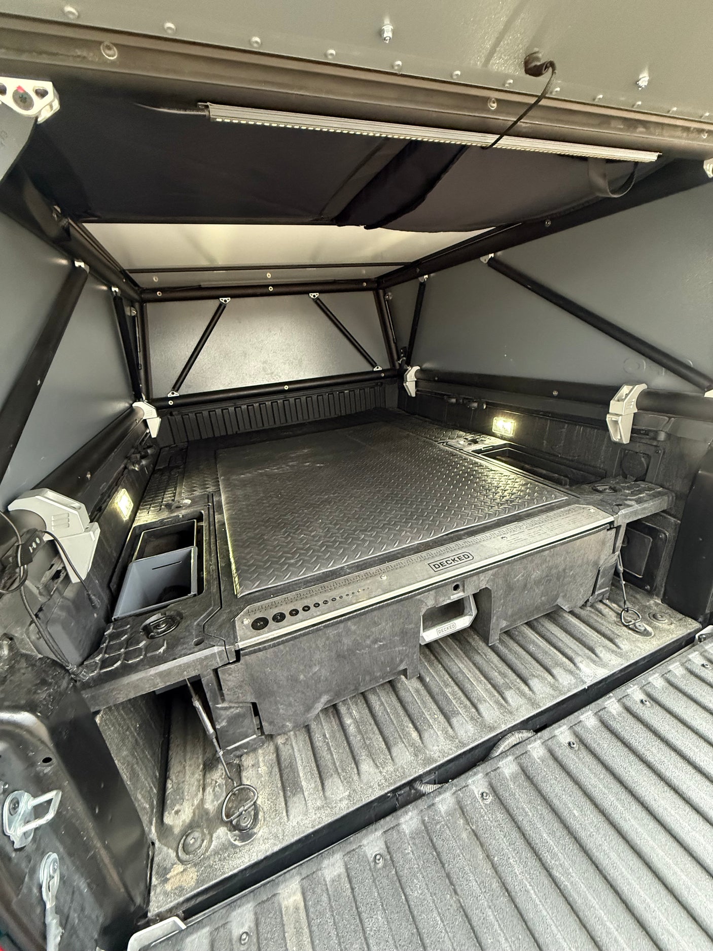 Truck bed camper setup for RV rental: Organized storage with DECKED system, bright LED lights, and soft-shell canopy.